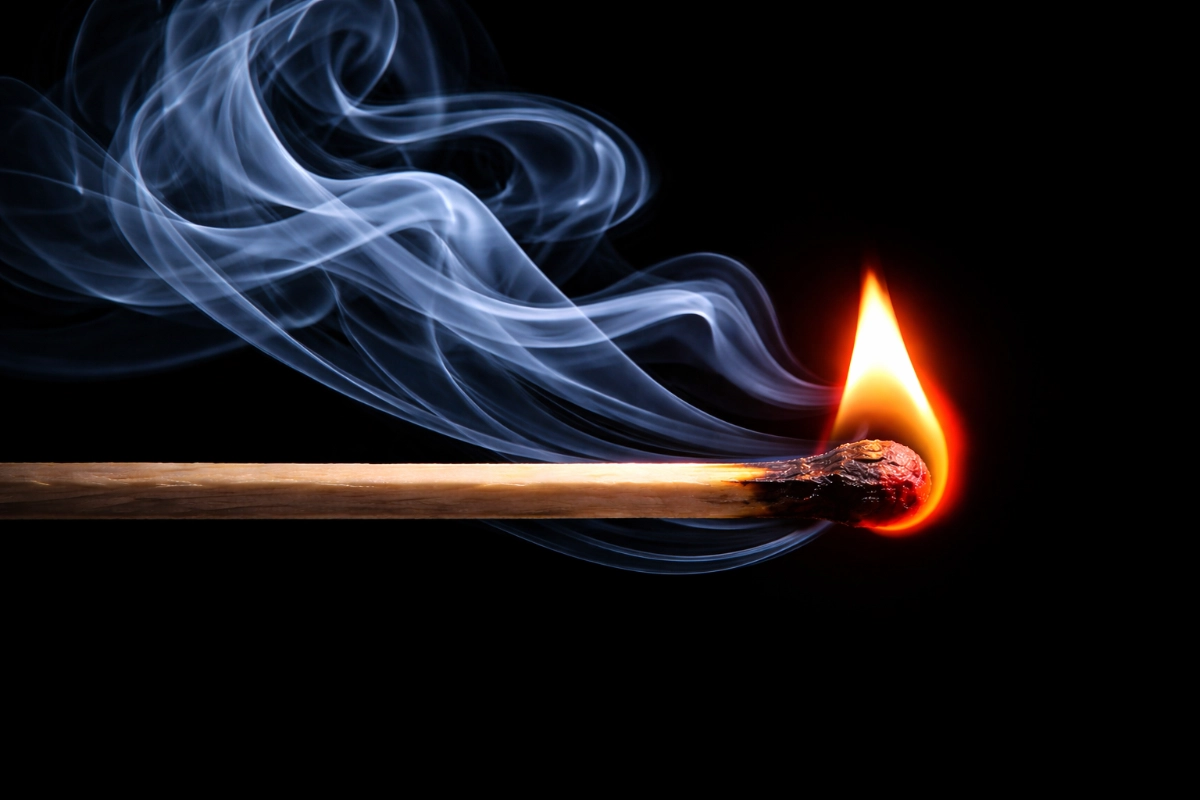 close up view of a lit match, with smoke trailing from the flame